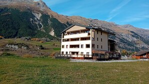 Ein zweistöckiges Gebäude mit Balkonen in einer gebirgigen Landschaft unter blauem Himmel.
