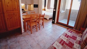 A compact living space with a kitchenette, a dining area, a bed, and a sliding glass door leading to a balcony. - Terrasses E 305 - PARC NAT. VANOISE appart. 6 pers (Val Cenis)