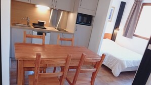 A compact kitchen with a microwave, sink, and stainless steel range hood. There is a wooden dining table with chairs and a bed with white bedding in the adjacent room. - Terrasses E 305 - PARC NAT. VANOISE appart. 6 pers (Val Cenis)