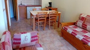 Een ruimtelijk ingerichte leefruimte met een kitchenette, een eethoek en een bank.