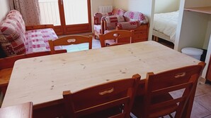 Een gezellige kamer met een houten eettafel, stoelen, een bank en een bed.