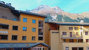 Ein gelbes Gebäude mit zahlreichen Fenstern und Balkonen, einem Schild mit der Aufschrift "Les Terrasses de Termignon" und einem Berg im Hintergrund.