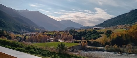 Un paisaje montañoso con un río, edificios y una baranda de madera.