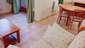 A cozy living area with a sofa, a wooden table, and chairs. A window with curtains is visible, and a radiator is mounted on the wall. - Terrasses D 309 - PARC NAT. VANOISE studio 4 pers (Val Cenis)