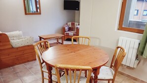 A dining area with a wooden table and chairs, a sofa, a TV, and a window with a view of buildings. - Terrasses D 309 - PARC NAT. VANOISE studio 4 pers (Val Cenis)