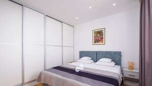 Ein modernes Schlafzimmer mit einer großen Schiebetür, einem Bett mit grauem Kopfteil, einem Nachttisch mit Lampe und einem gerahmten Bild an der Wand.