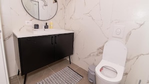 Ein Badezimmer mit einer weißen Toilette, einem schwarzen Schrank, einer Marmor-Spritzschutzwand und einem gemusterten Teppich.