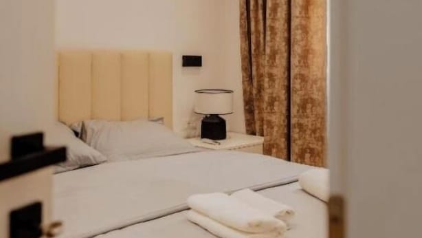 Ein Hotelzimmer mit einem Doppelbett, einem Nachttisch mit Lampe und einem Fenster mit Vorhängen.