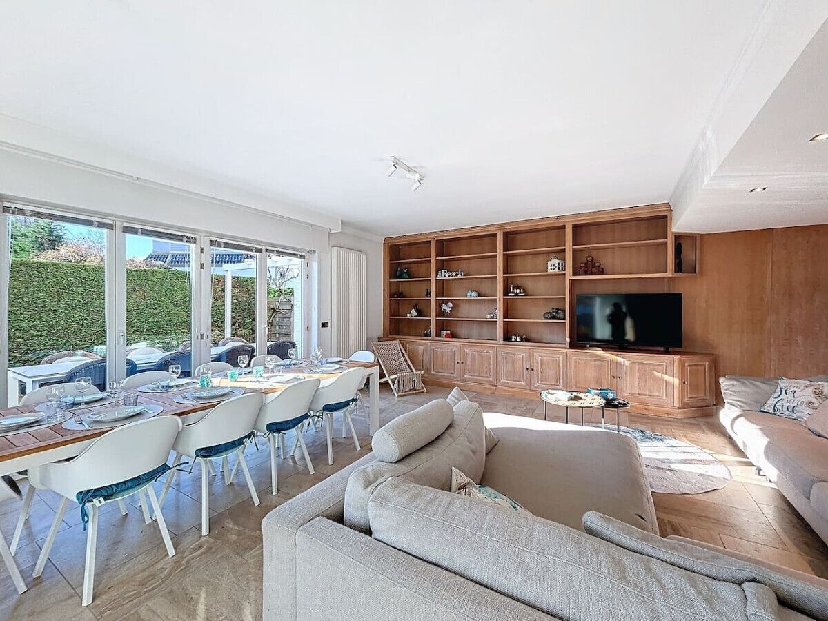 A spacious living area with a dining setup, a large TV, and a wooden cabinet.