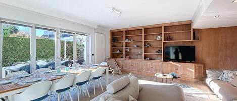 A spacious living area with a dining setup, a large TV, and a wooden cabinet.