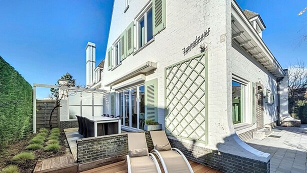 Una casa moderna con una terrazza, posti a sedere all'aperto e una grande finestra.