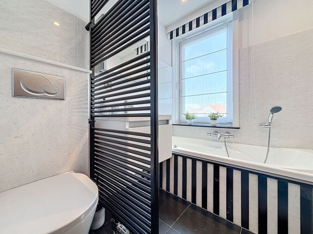 A modern bathroom with a toilet, a black and white striped shower enclosure, and a window with a view of the outside.