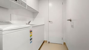 A small, white kitchen with a washing machine, a sink, and a door with a handle. - Aquaview Unit 604, 29 Canberra Tce, Kings Beach (Kings Beach)