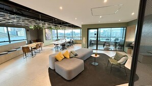 Een moderne kantoorruimte met een grote grijze bank, een klein rond tafeltje en een zithoek met stoelen.