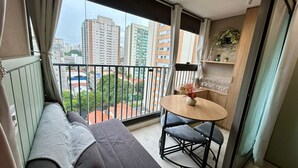 Een balkon met een bank en een kleine tafel, met uitzicht op gebouwen en een hekwerk.