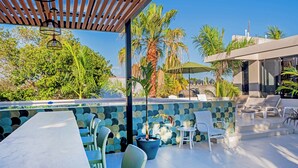 Een terras buiten met een zwembad, loungesessels en een eethoek met tafels en stoelen.