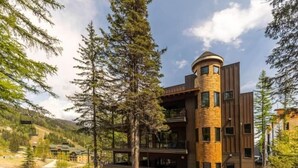 A modern building with a cylindrical tower, surrounded by trees and a mountainous landscape.
