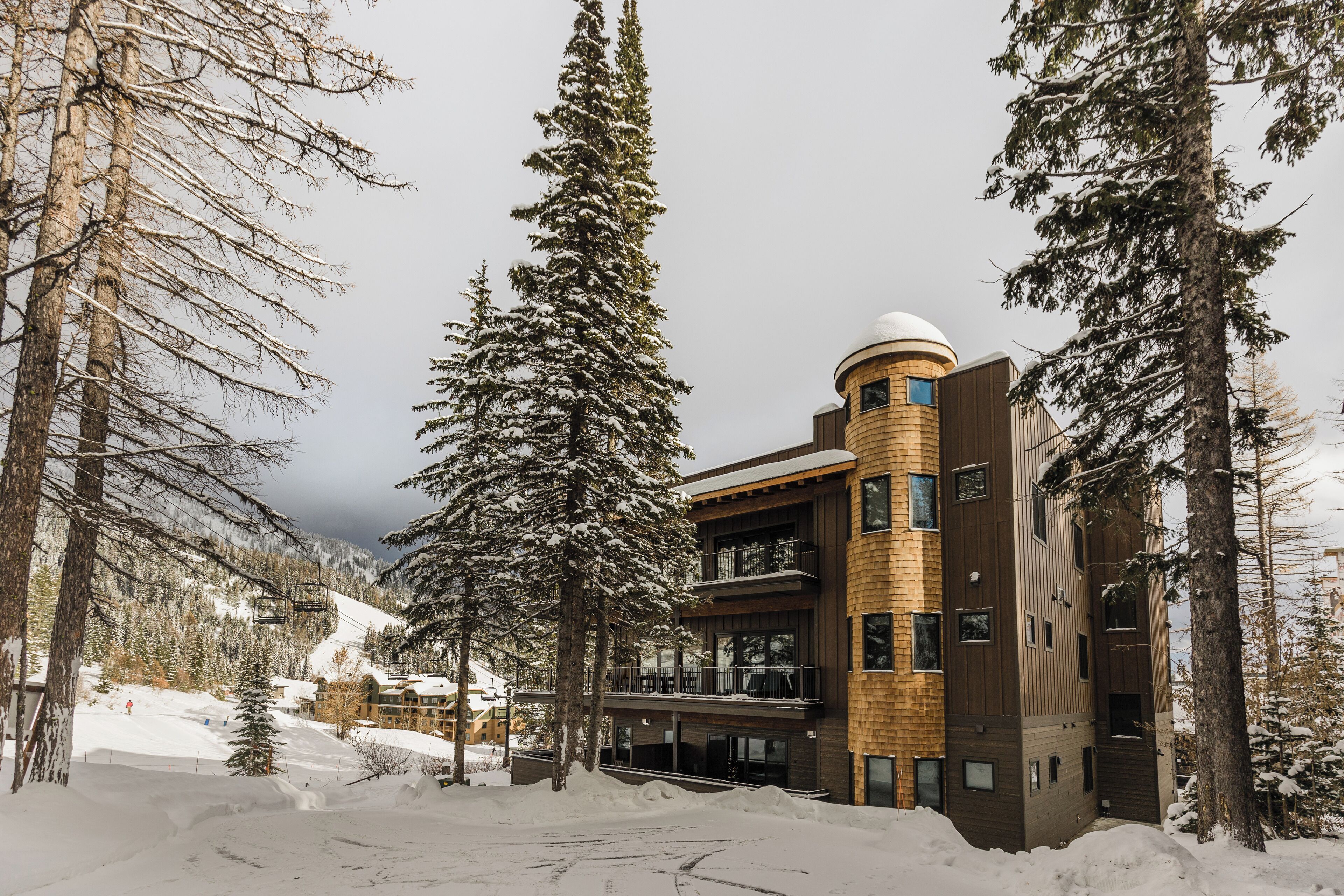A modern building with a ski lift in the background, surrounded by snow-covered trees.
