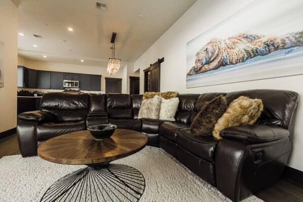 A modern living room with a leather sectional sofa, a round wooden coffee table, and a large abstract painting on the wall.