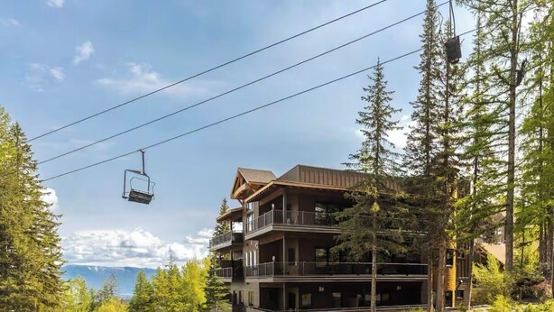 A multi-story lodge with a ski lift in the background, surrounded by trees and mountains.