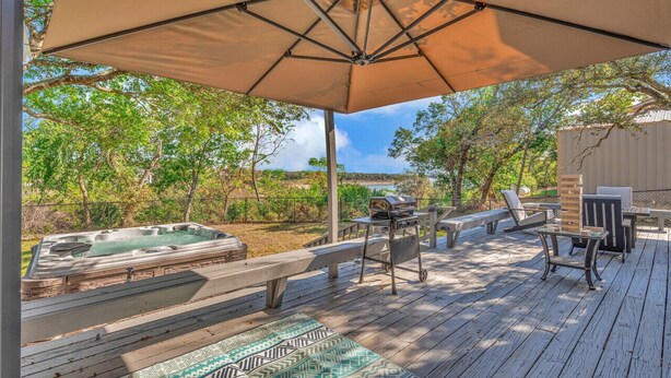 Eine Holzterrasse mit Whirlpool, Gartenmöbeln und einem großen Sonnenschirm.