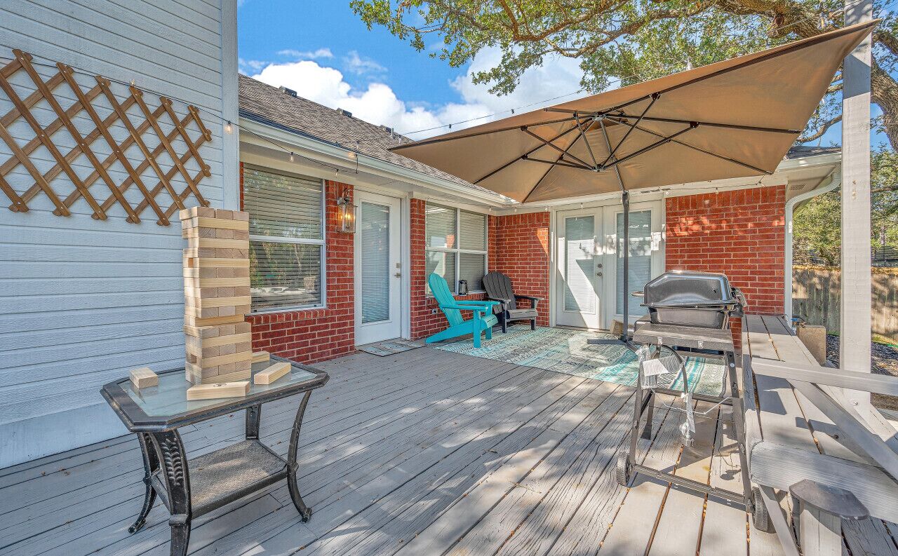 A covered patio with a grill, a table, and a chair.