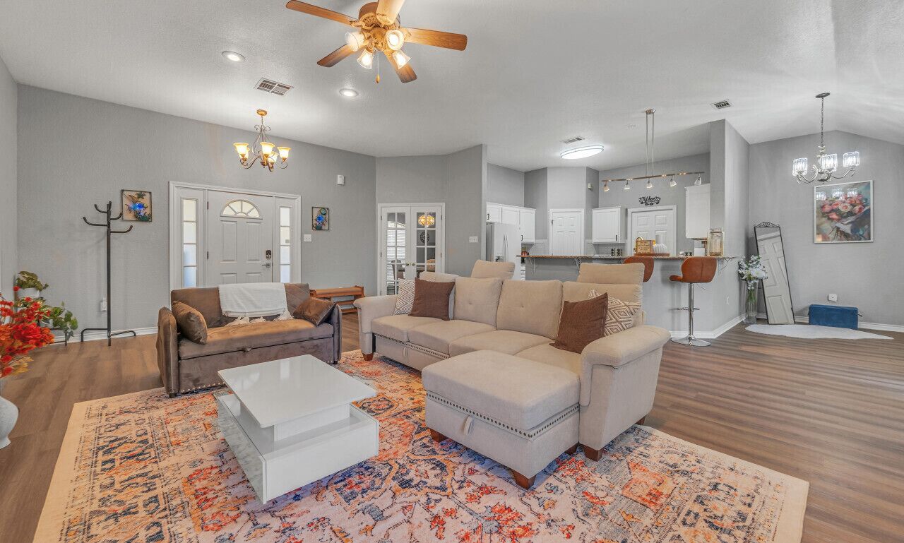A spacious living room with a large sofa set, a coffee table, and a dining area with a kitchen in the background.