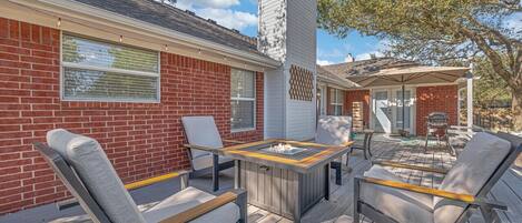 A patio with a fire pit, outdoor seating, and a brick building with large windows.