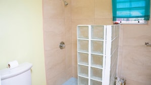 Un baño con ducha, inodoro y ventana con cortina.