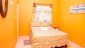 Una habitación con cama, ventana con cortinas, un cuadro en la pared y un espejo circular.