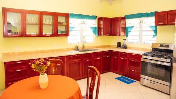 Una cocina con armarios de madera, una estufa y una mesa de comedor con un jarrón de flores.
