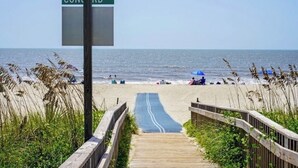 A beach with a wooden boardwalk leading to the ocean, a street sign reading 'CONCORD ST', and beachgoers in the distance. - Carolina Tide!5⭐️ Canal Front-Private Pool!Dock,Tiki Bar and Steps to the Beach! (Ocean Isle Beach)