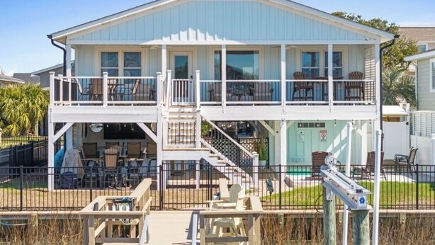A two-story house with a balcony, a covered patio, and a pool. - Carolina Tide!5⭐️ Canal Front-Private Pool!Dock,Tiki Bar and Steps to the Beach! (Ocean Isle Beach)