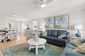 A living room with a sofa, coffee table, and chairs. There are two paintings on the wall, a ceiling fan, and a lamp. - 5⭐️ Canal Front-Pool!Dock,Tiki Bar and Steps to the Beach! (Ocean Isle Beach)