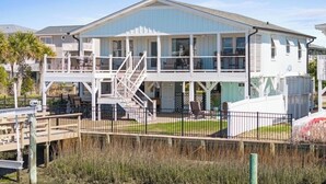 A two-story house with a balcony, a staircase, and a fenced yard. - Carolina Tide!5⭐️ Canal Front-Private Pool!Dock,Tiki Bar and Steps to the Beach! (Ocean Isle Beach)