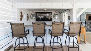 A bar area with three wicker chairs, a flat-screen TV, and decorative mirrors. - Carolina Tide!5⭐️ Canal Front-Private Pool!Dock,Tiki Bar and Steps to the Beach! (Ocean Isle Beach)