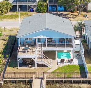 A two-story house with a pool, outdoor seating, and a fenced yard. - 5⭐️ Canal Front-Pool!Dock,Tiki Bar and Steps to the Beach! (Ocean Isle Beach)