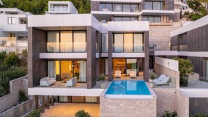 A modern multi-story residential building with a central courtyard featuring a swimming pool, outdoor seating, and a well-maintained garden. - Luxury Villa Beyond Waves with Pool (Baška Voda)