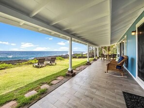 Un patio techado con vista al océano, mobiliario exterior y un área con césped.