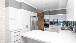 A modern kitchen with white cabinetry, a stainless steel refrigerator, and a brick accent wall. - Oceans Edge - Spectacular home with ocean views on the hill of Mollymook Beach (Mollymook Beach)