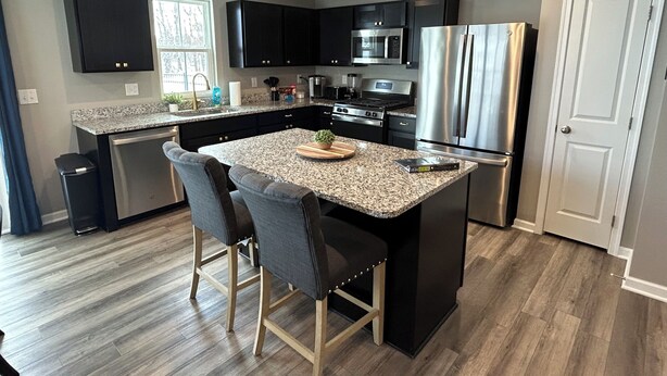 A modern kitchen with a granite countertop, stainless steel appliances, and a central island with bar stools.