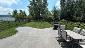 A patio area with a curved concrete floor, a grill, and a table with chairs.