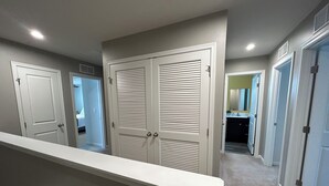 A hallway with white doors, a visible bathroom with a mirror, and a carpeted floor.