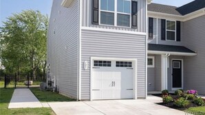 A two-story house with a white garage door, a small front porch, and a mailbox.