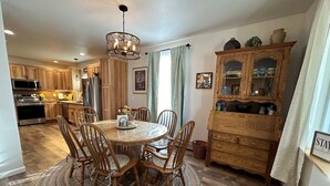 Un coin repas avec une table ronde, des chaises en bois, un lustre et un buffet en bois doté de portes en verre.