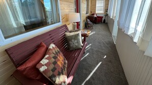 L’intérieur chaleureux d’un chalet avec un banc en bois, une table avec une lampe et un fauteuil rouge.