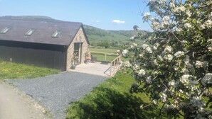 A stone building with a sloped roof, a wooden deck, and a view of green hills. - The Barn @ Tyn y Ffridd , great views,
 WiFi, log burner (Denbighshire)