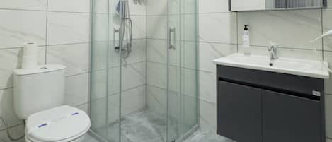 Un bagno moderno con cabina doccia in vetro, un water e un lavandino con specchio sopra.
