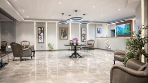 A modern lobby with a marble floor, leather seating, a central table with a vase, and a TV on the wall. - Altınova Hotel Sakarya  (Serdivan)