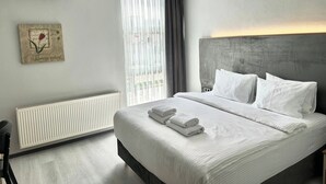 A modern hotel room with a large bed, white linens, a radiator, and a window with blinds. - Altınova Hotel Sakarya  (Serdivan)